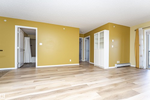 Open concept living space featuring wood-finish flooring, white baseboards, and bright yellow walls - 404 12045 22 Avenue, Edmonton, AB 