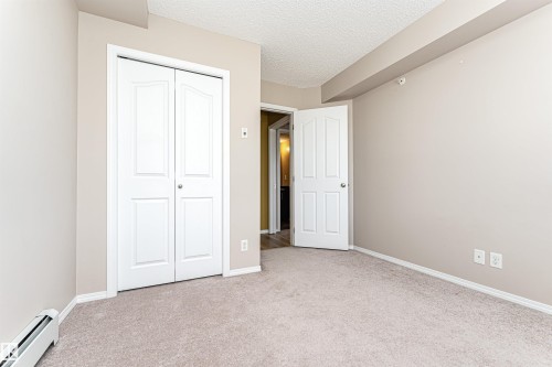 Neutral-toned carpeted room featuring a white bi-fold closet door with panel detailing, a white paneled interior door, and baseboard trim - 404 12045 22 Avenue, Edmonton, AB 
