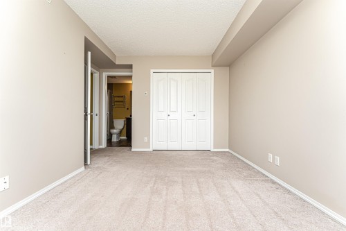 Carpeted room with neutral wall paint and white baseboards - 404 12045 22 Avenue, Edmonton, AB 