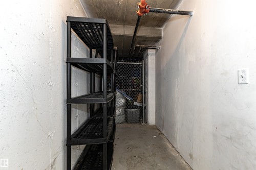 Utility space featuring a stacked shelving unit, concrete flooring, and exposed ceiling utilities - 404 12045 22 Avenue, Edmonton, AB 