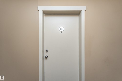 Entry door with contemporary silver-toned hardware and white trim, set against a neutral wall - 404 12045 22 Avenue, Edmonton, AB 