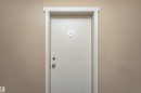 Entry door with contemporary silver-toned hardware and white trim, set against a neutral wall - 404 12045 22 Avenue, Edmonton, AB 
