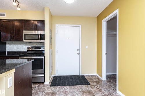 Entryway featuring tiled flooring, a built-in closet with shelving, and a kitchen with dark cabinetry, stainless steel appliances, and a tiled backsplash - 404 12045 22 Avenue, Edmonton, AB 