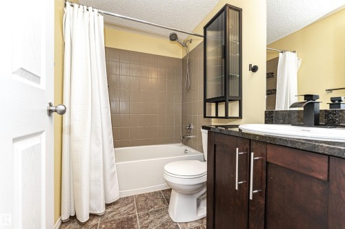 Bathroom featuring a white tub and shower combination with brown wall tiling - 404 12045 22 Avenue, Edmonton, AB 