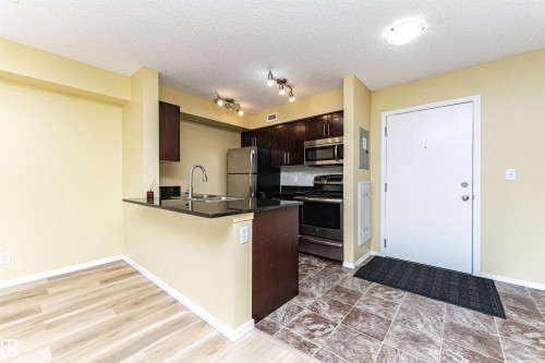 Compact kitchen featuring dark wood cabinetry, stainless steel appliances, black countertops, and a white subway tile backsplash - 404 12045 22 Avenue, Edmonton, AB 