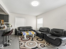 Open-concept living space featuring wood-finish flooring, white walls, and multiple windows with roller blinds - 