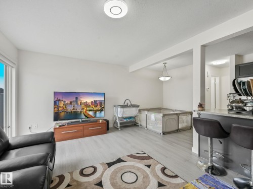 Open-concept living area featuring light wood-finish flooring, white walls, a recessed ceiling light, and a modern pendant light - 18 230 Edwards Drive, Edmonton, AB 