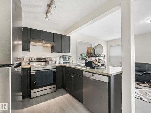 Modern kitchen featuring dark cabinetry, stainless steel appliances, wood-finish flooring, track lighting, and a light-toned countertop - 18 230 Edwards Drive, Edmonton, AB 