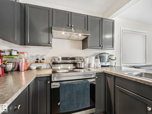 Kitchen featuring dark gray cabinetry with silver hardware, stainless steel range with overhead ventilation, light-toned countertops, and a stainless steel sink - 18 230 Edwards Drive, Edmonton, AB 