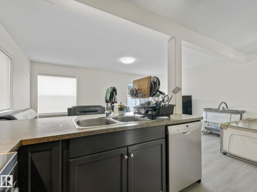 Kitchen island with dark cabinetry, dual stainless steel sinks, and a light-toned countertop - 18 230 Edwards Drive, Edmonton, AB 