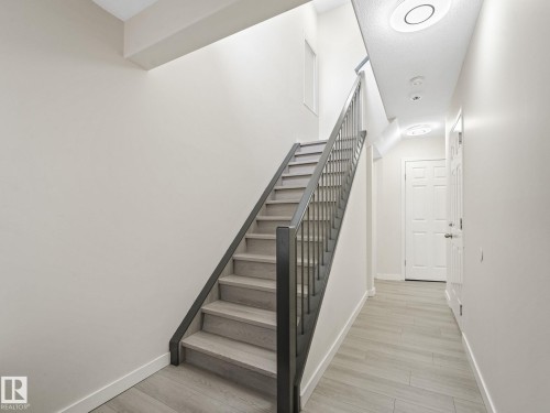 Contemporary staircase featuring wood-finish treads and risers, black metal balusters, and a matching handrail - 18 230 Edwards Drive, Edmonton, AB 