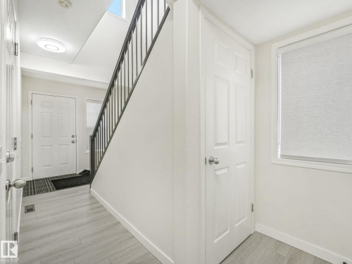 Entryway featuring light wood-finish flooring and a staircase with dark metal railings - 18 230 Edwards Drive, Edmonton, AB 