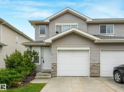 Grey siding exterior with a white front door, stone accents, attached garage, and concrete driveway - 