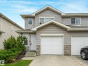 Grey siding exterior with a white front door, stone accents, attached garage, and concrete driveway - 18 230 Edwards Drive, Edmonton, AB 
