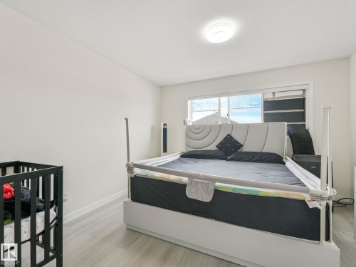 Bedroom with light wood-finish flooring, white walls, and a large window - 18 230 Edwards Drive, Edmonton, AB 