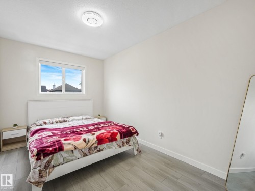 Bedroom featuring light wood-finish flooring, white walls, and a large window with white trim - 18 230 Edwards Drive, Edmonton, AB 