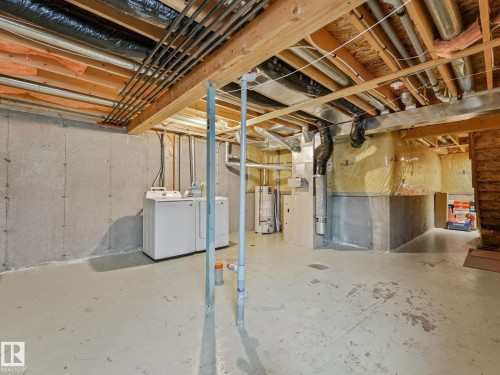 Unfinished basement featuring exposed joists, concrete walls, and a painted concrete floor - 18 230 Edwards Drive, Edmonton, AB 