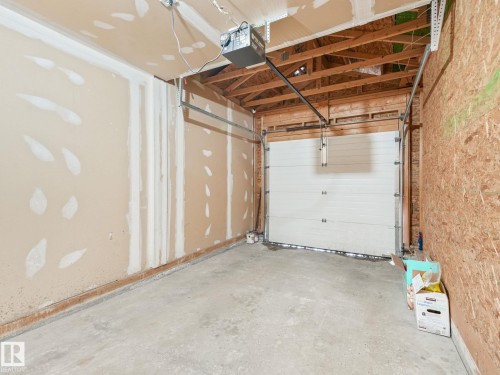 Garage featuring an automatic overhead door, concrete flooring, and exposed ceiling joists - 18 230 Edwards Drive, Edmonton, AB 