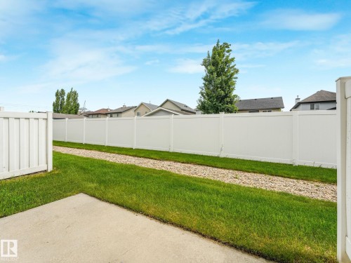 Expansive backyard featuring a white vinyl privacy fence, concrete patio area, and a gravel strip separating areas of green lawn - 18 230 Edwards Drive, Edmonton, AB 