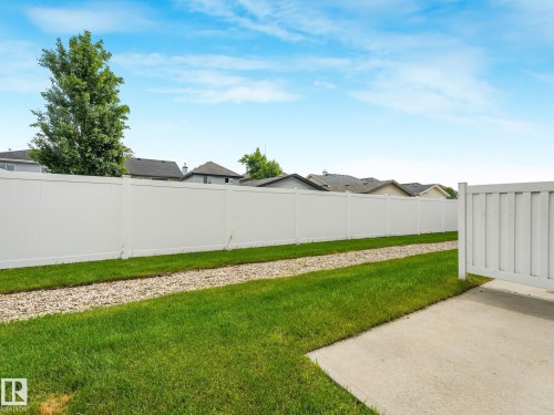Expansive backyard featuring a full-height white privacy fence, a concrete patio, a gravel border, and a manicured lawn - 18 230 Edwards Drive, Edmonton, AB 