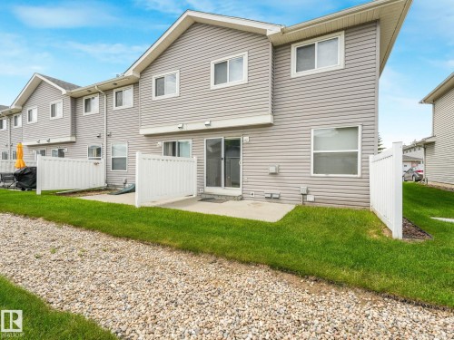 Rear exterior featuring gray horizontal siding, multiple windows, and a sliding glass door - 18 230 Edwards Drive, Edmonton, AB 