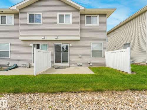 Rear exterior with light gray siding, concrete patio, white vinyl fencing, and a sliding glass door - 18 230 Edwards Drive, Edmonton, AB 