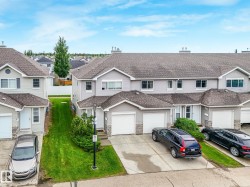 Townhome exterior featuring light gray siding, dark shingle roofing, white garage doors, and stone facade accents - 