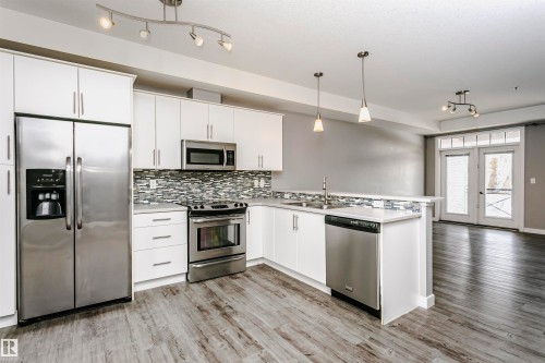 Modern kitchen featuring white cabinetry, stainless steel appliances, a tile backsplash, light countertops, and wood-finish flooring - 211 10808 71 Avenue, Edmonton, AB 
