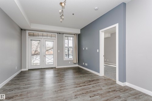 Spacious room featuring wood-finish flooring, a contemporary track lighting fixture, and a feature wall in a contrasting tone - 211 10808 71 Avenue, Edmonton, AB 