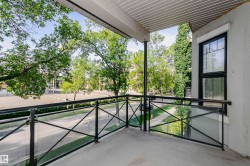 Private balcony featuring a concrete floor, black metal railing with glass inserts, and an overhead soffit - 