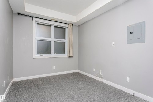 Room featuring a frosted pane window with white trim, light gray wall paint, gray carpet flooring, white baseboards, and a tray ceiling detail - 211 10808 71 Avenue, Edmonton, AB 