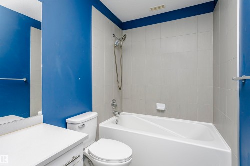 Bathroom featuring a white bathtub, tiled shower surround, wall-mounted shower head, white toilet, and a white vanity with integrated sink - 211 10808 71 Avenue, Edmonton, AB 