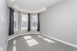 Room with a multi-pane bay window, neutral gray walls, light gray carpeting, and white baseboards - 