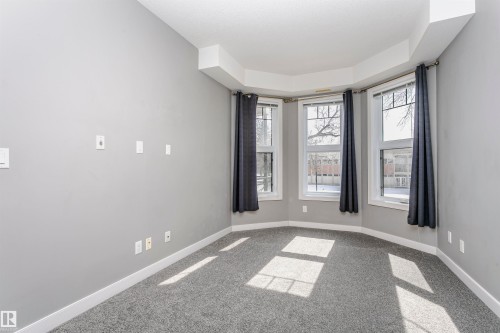 Bay window with three individual windows, light gray walls, dark gray carpeting, and white baseboards - 211 10808 71 Avenue, Edmonton, AB 