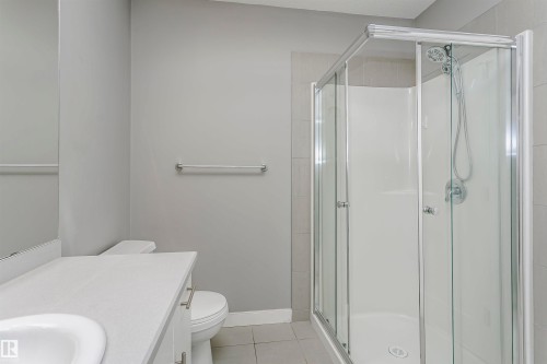 Corner glass-enclosed shower with white surround, complemented by a white vanity with an integrated sink and base cabinetry - 211 10808 71 Avenue, Edmonton, AB 