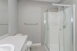 Corner glass-enclosed shower with white surround, complemented by a white vanity with an integrated sink and base cabinetry - 