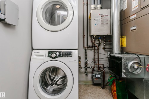 Dedicated utility area featuring a stacked washer and dryer unit, wall-mounted tankless water heater, and a furnace - 211 10808 71 Avenue, Edmonton, AB 