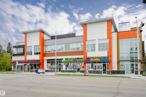 Modern commercial building featuring multiple storefronts, a prominent orange and white facade, expansive window displays, contemporary architectural lines, and a visible street-front presence - 211 10808 71 Avenue, Edmonton, AB 
