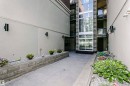 Exterior walkway featuring concrete paving, stone retaining walls, and a multi-story glass elevator shaft with stone detailing - 211 10808 71 Avenue, Edmonton, AB 