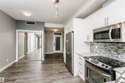 Modern kitchen featuring white cabinetry, stainless steel appliances, a mosaic tile backsplash, and light-toned countertops - 