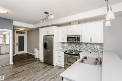 Modern kitchen featuring white cabinetry, stainless steel appliances, a mosaic tile backsplash, a double basin sink, and light-toned countertops - 