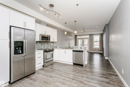 Modern kitchen featuring white cabinetry, stainless steel appliances, a mosaic tile backsplash, and wood-finish flooring - 211 10808 71 Avenue, Edmonton, AB 