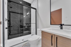 Bathroom featuring a black-framed glass shower enclosure, black-veined wall tile, a wood-finish vanity with a white countertop, and a contemporary black faucet - 