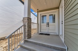 Entryway featuring double doors with decorative glass panels, a stone-accented column, concrete steps with exposed aggregate risers, and a metal handrail - 