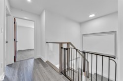 Upper-level landing featuring wood-finish flooring, a glass and metal staircase railing, recessed lighting, a framed wall accent, and a solid-core interior door - 