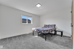 Bright room featuring a square window, neutral wall paint, gray carpeting, a flat panel ceiling light, and a wooden door with a black handle - 