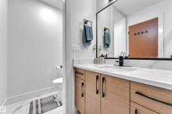 Bathroom featuring a wood-finish vanity with black hardware, white countertop, and a black-framed mirror - 