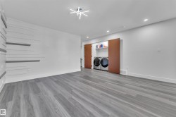 Spacious laundry area featuring wood-finish flooring, a contemporary ceiling light fixture, recessed lighting, and a built-in laundry closet with sliding doors - 