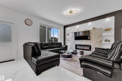 Spacious living area featuring large format white tile flooring with subtle gray veining, a decorative fireplace with a stone-finish facade, built-in shelving with recessed lighting, and a contemporary ceiling light fixture - 