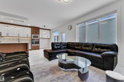 Open-concept living space featuring a contemporary kitchen with white and wood-finish cabinetry, integrated appliances, and a decorative tile backsplash - 
